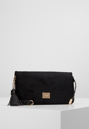Sac matelassé noir en suède avec une plaque dorée et un détail de pampille. Il dispose d'une bandoulière en chaîne et d'une texture lisse.