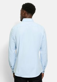 Hellblaues Langarmhemd mit spitzem Kragen, glatter Textur und schwarzen Knopfakzenten an den Manschetten, von hinten betrachtet.