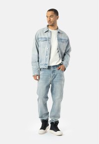 Lyseblå denimjakke med slidte detaljer, parret med lyseblå jeans og sorte high-top sneakers. Hvid skjorte underneath.