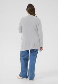 Maglione oversize grigio chiaro con orlo e polsini a coste, abbinato a jeans di denim blu a gamba larga. Texture liscia e vestibilità rilassata.