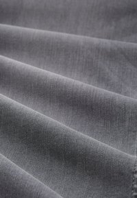 Szary materiał tekstylny o gładkiej fakturze, pofałdowany. Widoczny subtelny wzór tkany, tworzący wyrafinowany, jednolity wygląd.