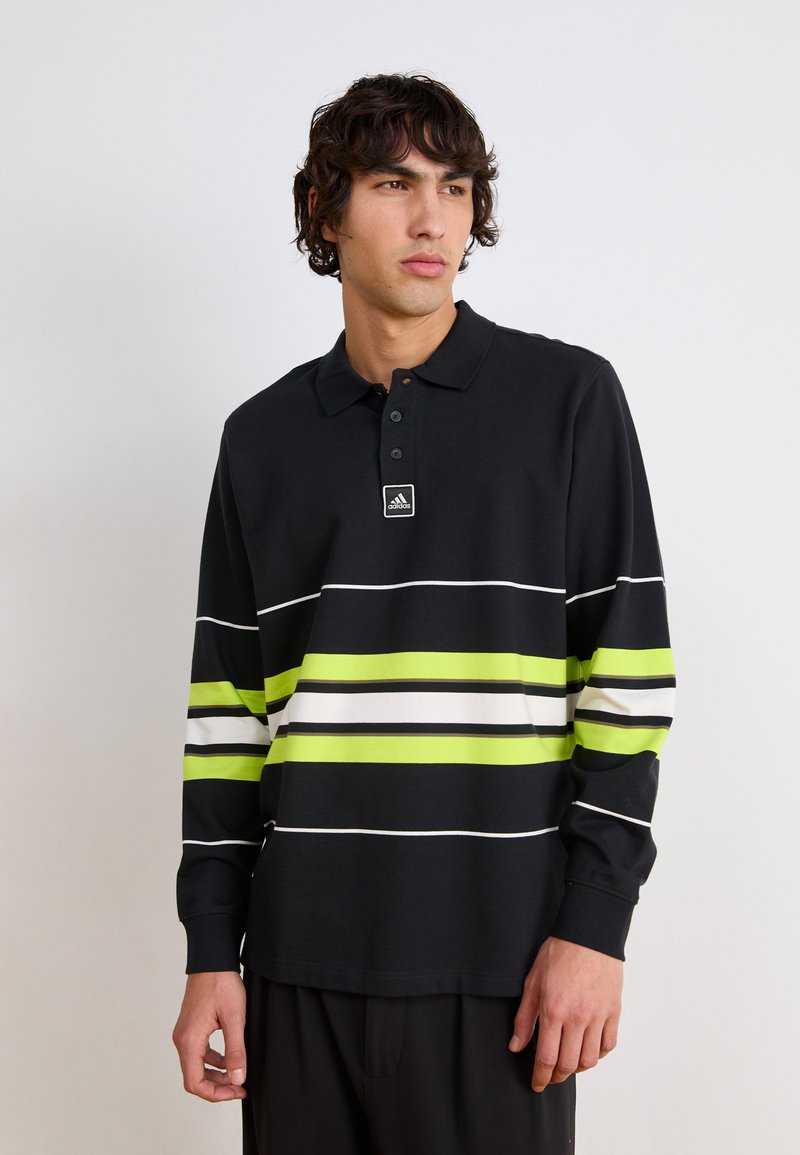 Polo à manches longues noir avec des rayures horizontales vertes, blanches et noires. Il présente un col et un petit logo sur la poitrine.