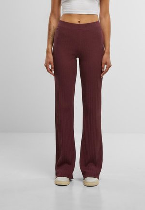 Ribbed, high-waisted pants in burgundy, featuring a flared leg design and a smooth texture. Worn with cream-colored sneakers.