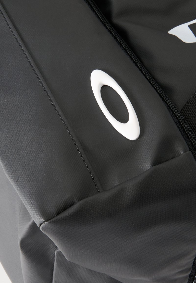 Weißes ovales Logo auf schwarzer, strukturierter Sporttasche mit sichtbarem Reißverschluss und Nahtdetails.