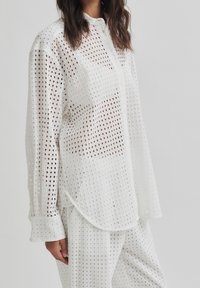 White shirt featuring a grid pattern, made of lightweight fabric, button-down front, long sleeves, and a rounded hemline.