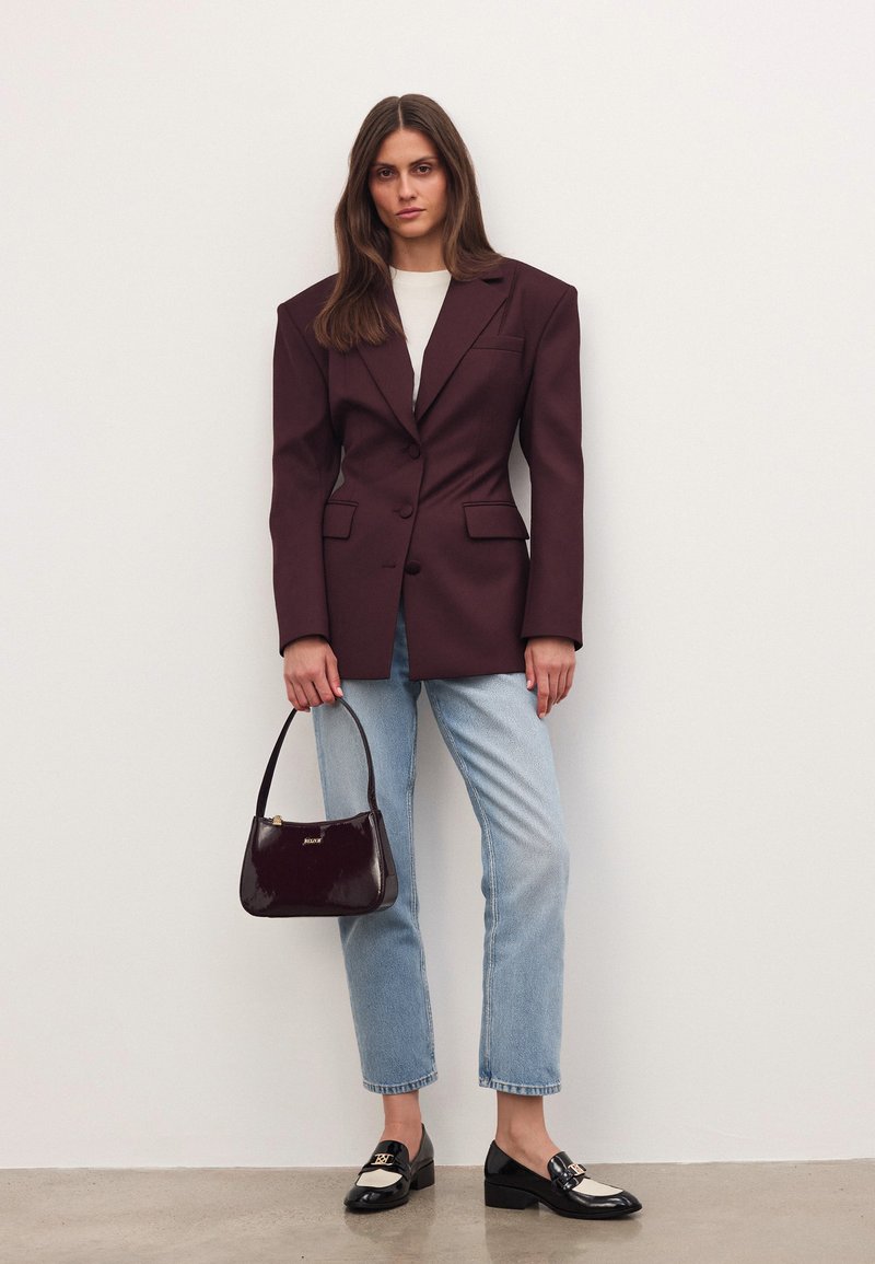 Bordeauxfärgad oversized blazer med strukturerade axlar, kombinerad med ljusblå raka jeans. Bär en glansig bourgognehandväska och har på sig svarta loafers.