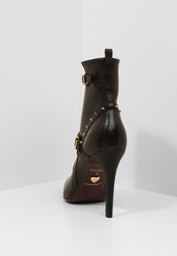 Bottines en cuir noir avec un talon aiguille, ornées d'accents en métal doré et de clous en forme de pyramide sur le côté, texture lisse.