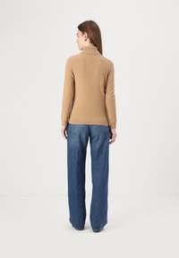 Kamelivärvi, istuv kõrge kaelusega sweater, pikkade varrukatega ja ribaga äärega, koos laia säärega siniste denimpükstega. Pehme tekstuur.