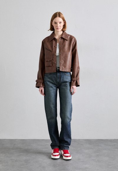 Brown faux leather cropped jacket with front pockets, paired with blue denim jeans and red and white sneakers. Textured material throughout.