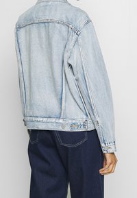 Ljusblå denimjacka med en blekt tvätt, med dubbelsydda sömmar, framknappar och en avslappnad passform. Bakdesignen är enkel.