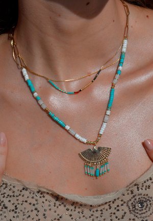 Collier superposé ton or avec des perles turquoise et blanches, orné d'un pendentif en forme d'éventail accentué par des perles pendantes au centre.