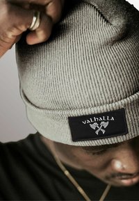 Gray ribbed beanie with a black tag featuring "valhalla" and crossed axe design. Fabric has a textured appearance.
