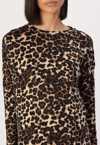 Langermet topp med leopardskrift på en beige bakgrunn, mørkebrune og sorte flekker, og et mykt, teksturert stoff.