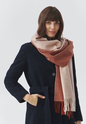 Herringbone-patterned scarf in soft materials, featuring a gradient from light pink to rust, with fringed edges. Worn over a dark coat.