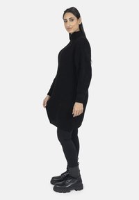 Sort ribstrikket sweaterekjole med høj hals, lange ærmer og sideslids, kombineret med sorte tætsiddende leggings og snørelige kampstøvler.