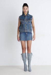 Ensemble en denim composé d'un gilet et d'une jupe de couleur bleu clair, avec des bords effilochés, associé à des bottes grises à lacets montant jusqu'aux genoux. Texture lisse, design structuré.