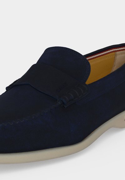 Σουέντ μοκασίνι ναυτικού μπλε με ραφές μοκασίνι, δερμάτινη επένδυση, ριγέ εσωτερική επένδυση και μπεζ καουτσούκ σόλα.