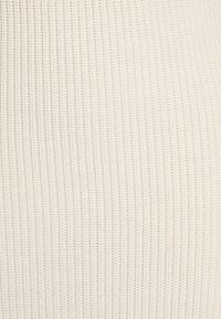 Ribbade stickade tyget i en ljus gräddfärg, med en strukturerad yta med vertikala linjer och ett mjukt, flexibelt utseende.