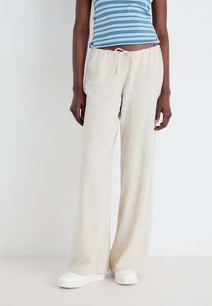 Beige linbukse med vide ben, elastisk midje og snor. Modellen har på seg hvite slip-on sko. Jevn tekstur, uformelt design.
