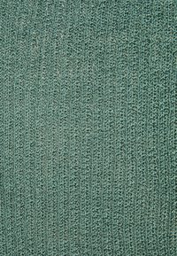 Zbliżenie na zieloną dzianinę, ukazujące szczegółową pętelkową teksturę i splecione wzory włókien.