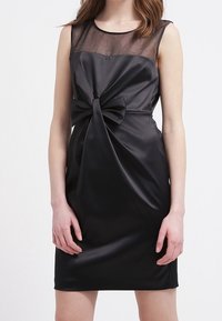 Robe en satin noir avec un décolleté transparent, ornée d'un nœud central à la taille et d'une silhouette ajustée. Texture lisse sur l'ensemble.