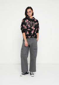 Czarna bluza w kwiatowy wzór z logo „GAP”, szare szerokie spodnie cargo oraz czarne trampki z białymi podeszwami; casualowy look na ulicę.