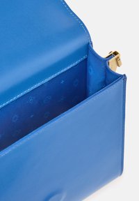 Interno di una borsa in pelle blu con finitura liscia, dotata di una chiusura dorata. La fodera interna mostra un motivo sottile di forme geometriche.