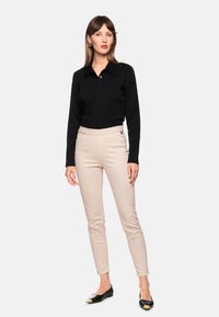 Black long-sleeve polo shirt with collar, light beige fitted pants, and black flats with gold accents, worn by a model against a light background.