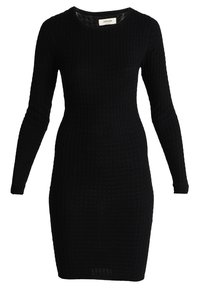 Robe noire en maille avec manches longues, présentant une texture côtelée et un col rond. Silhouette moulante avec une longueur mi-cuisse.