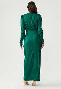 Lång grön satin klänning med åtsittande midja, puffärmar och dragkedjedetalj i ryggen. Slät textur, golvlång design med rak silhuett.