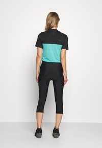 Conjunto de ciclismo negro y verde azulado que presenta una camiseta de manga corta con un diseño a rayas y un pantalón ajustado con un asiento de ciclismo acolchado.