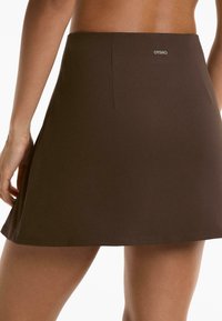 Brown skater skirt with a smooth texture, above-the-knee length, and subtle logo detail at the waist. Suitable for casual wear.
