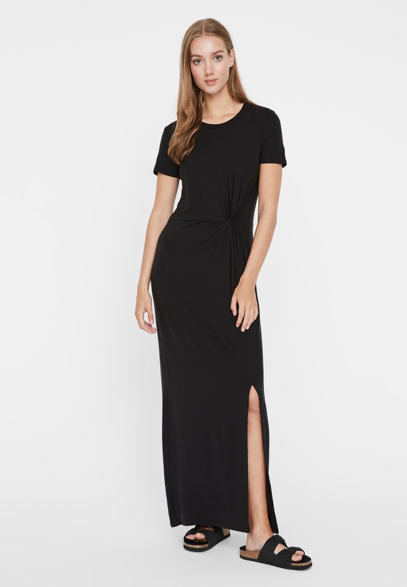 Μαύρο μάξι φόρεμα από μαλακό υλικό, με στρογγυλή λαιμόκοψη, κοντά μανίκια και σχισμή στο πλάι. Συνδυασμένο με μαύρα σανδάλια.