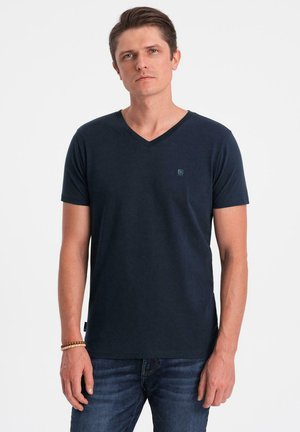 Marinblå v-neck t-shirt i mjukt material, med en liten logga på bröstet och korta ärmar, tillsammans med mörka jeans.