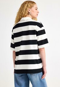 Stribet sort-hvid kortærmet skjorte med krave, der har en afslappet pasform og blød tekstur. Blå denim jeans bæres sammen med den.