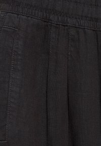 Gros plan d'un tissu noir avec des coutures visibles et des plis, montrant la texture et les coutures d'un vêtement.