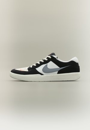 Lave sorte og hvite sneakers med grå Nike Swoosh, hvite lisser og beige såle, vist i venstre profil mot grå bakgrunn.
