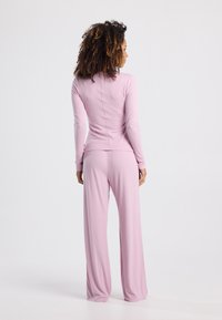 Long-sleeved, fitted top and wide-leg pants in soft, light pink fabric. Seam detailing along the back with a smooth, lightweight texture.
