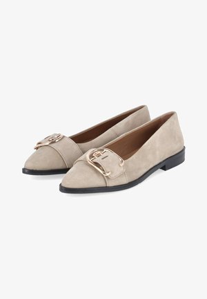 Beige suède platte schoenen met puntige neus, grote goudkleurige metalen gespen en zwarte zolen, getoond als een paar schuin naar links.