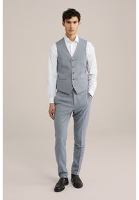 Chaleco texturizado gris claro con cinco botones, combinado con pantalones a juego. Camisa blanca debajo. Zapatos negros sin cordones. Diseño simple y ajustado.