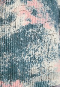 Tessuto lavorato a maglia in teal e rosa con un motivo sfocato, caratterizzato da accenti metallici e una texture a coste, che mostra forme astratte e scritte.