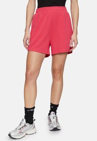 Pantalones cortos deportivos rosa con cinturilla elástica, hechos de una tela suave. Cuenta con bolsillos laterales y un detalle de logo en el muslo izquierdo.