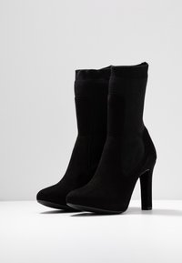 Botines negros con tacón alto, fabricados en un suave material de ante, con paneles laterales elásticos y un diseño de punta redonda suave.