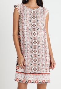 Robe fleurie en tissu léger avec un décolleté rond, des manches courtes et un motif symétrique en rose, noir et blanc. Présente un ourlet contrastant.