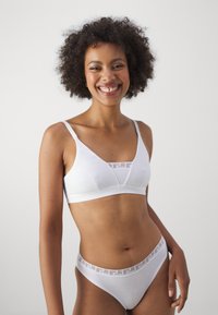 White lingerie set featuring a soft bralette and matching thong. Bra has thin straps and a decorative band; thong has a patterned waistband.