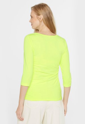 Neon-gelbes, enganliegendes Langarmoberteil mit rundem Ausschnitt. Der Stoff ist glatt und dehnbar und hat Ärmel in Dreiviertellänge.