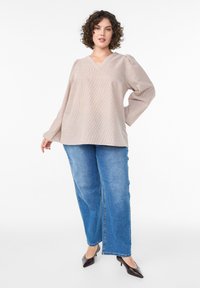 Svetlá béžová blúzka s dlhým rukávom, textúrovanou látkou, výstrihom do V a nafúknutými rukávmi, doplnená svetlomodrými rovným strihom džínsy a čiernymi opätkami.