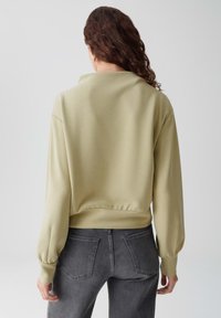 Felpa verde oliva con una vestibilità comoda, orlo a costine e maniche a palloncino, abbinata a jeans grigi scuri a vita alta.