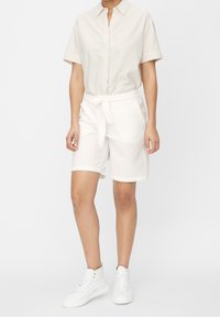 Shorts blancs texturés avec une taille à nouer, associés à une chemise à manches courtes à rayures claires. Complétés par des baskets montantes blanches.