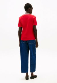 Rode t-shirt met korte mouwen en een ronde halslijn, gecombineerd met losse blauwe denim jeans en zwarte platte schoenen, gezien vanuit de achterkant.